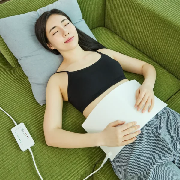 abdomen-irradiator-laying-down Woman receiving red light therapy at home, lying with the Abdomen Irradiator mat on her stomach for PBM therapy.