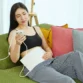 Woman sitting with the Abdomen Irradiator mat on her stomach, adjusting settings on the controller for red light therapy.